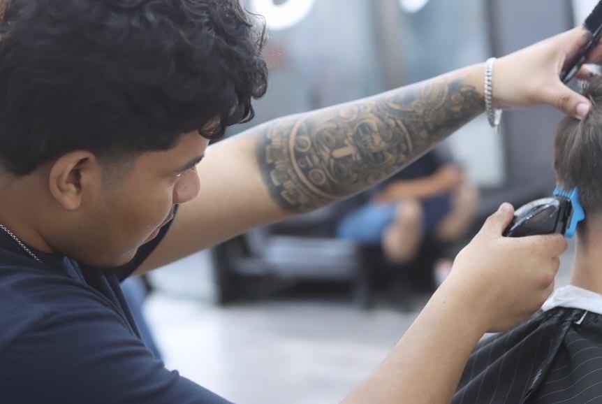 Barber with a tattooed forearm cutting a client's hair with clippers